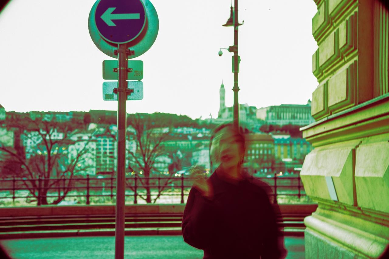 A figure in red under a street sign, the colours pushed to green and magenta