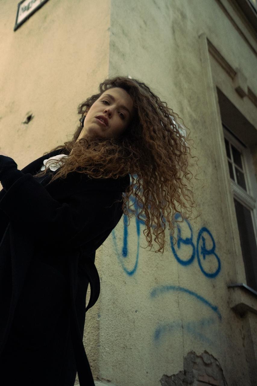 A woman with curly hair leaning on a wall with graffiti