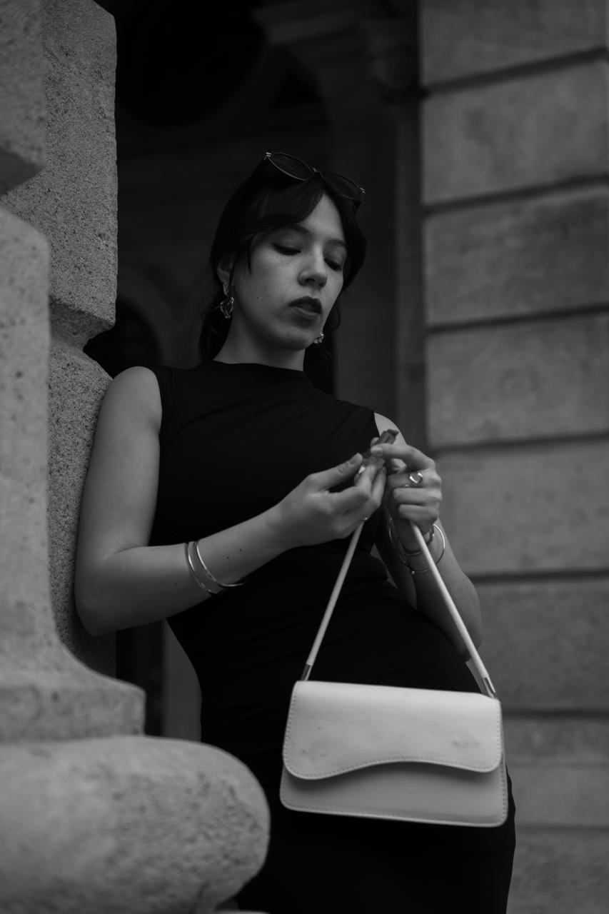 A woman with a white handbag by a stone column, in black and white