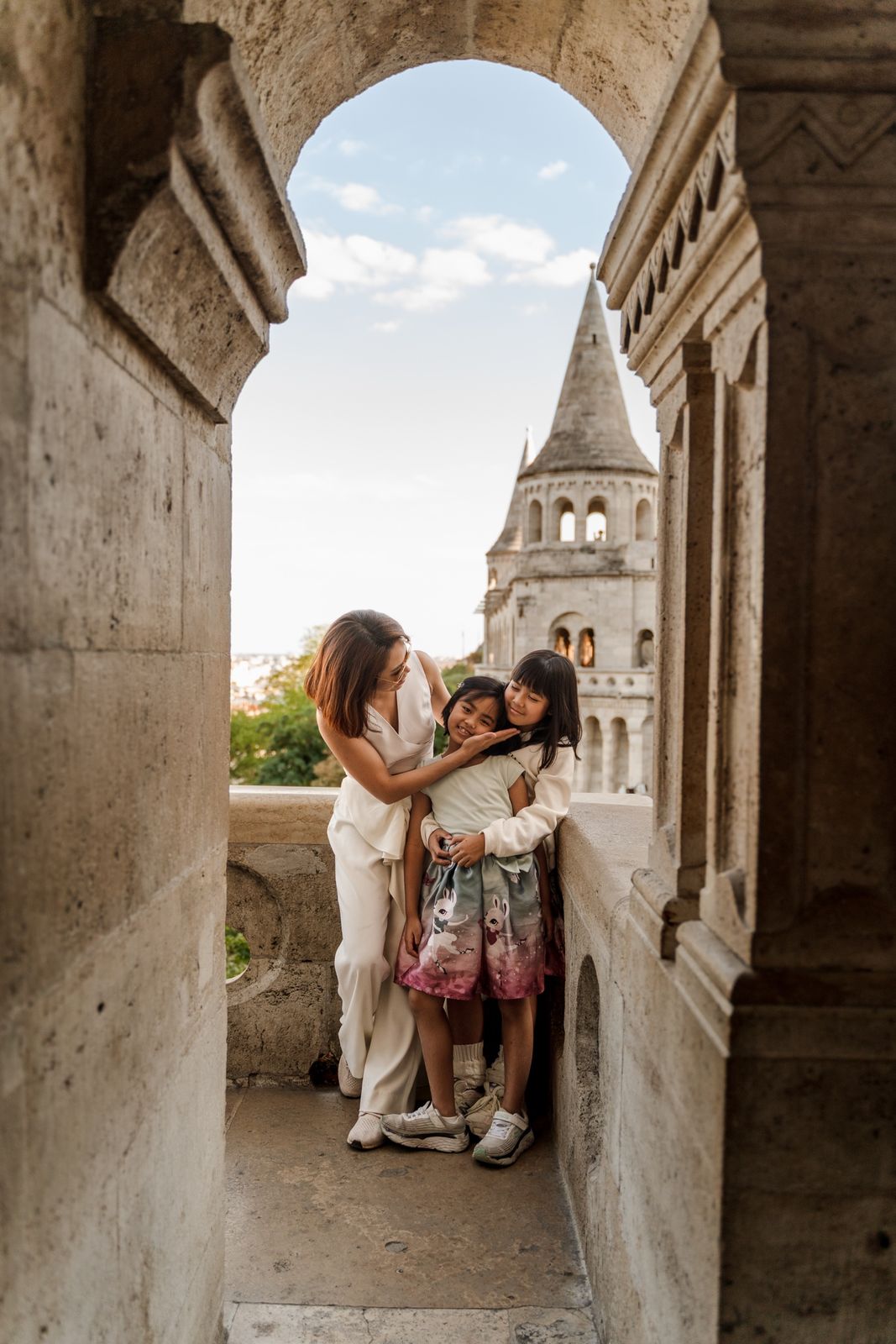 A mother hugging her two daughters inside an arch of Fisherman's Bastion