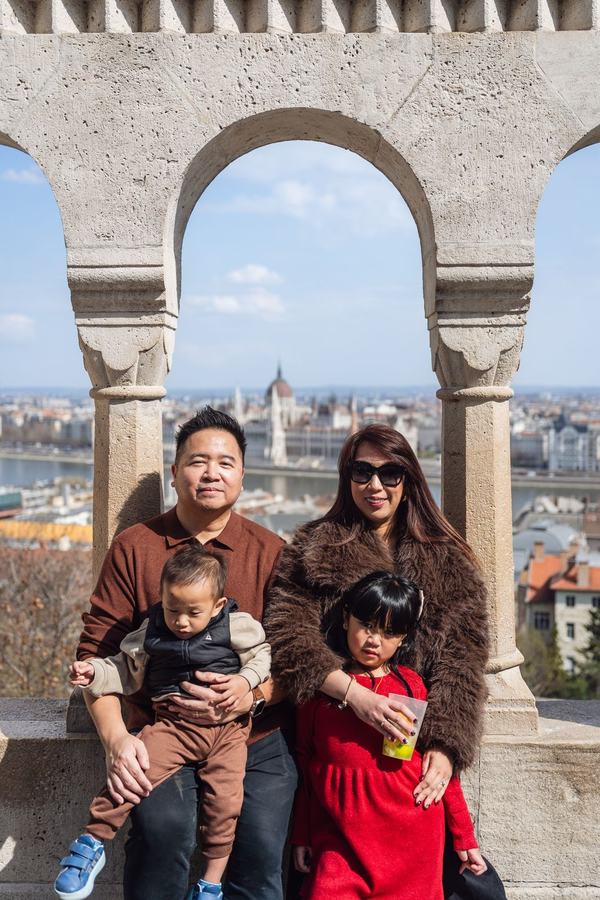 A family framed by a stone arch at Fisherman's Bastion, the Parliament behind them