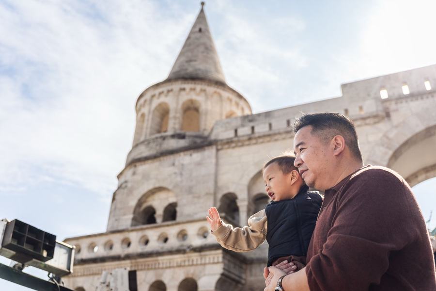 A father holding his waving son below a tower of Fisherman's Bastion