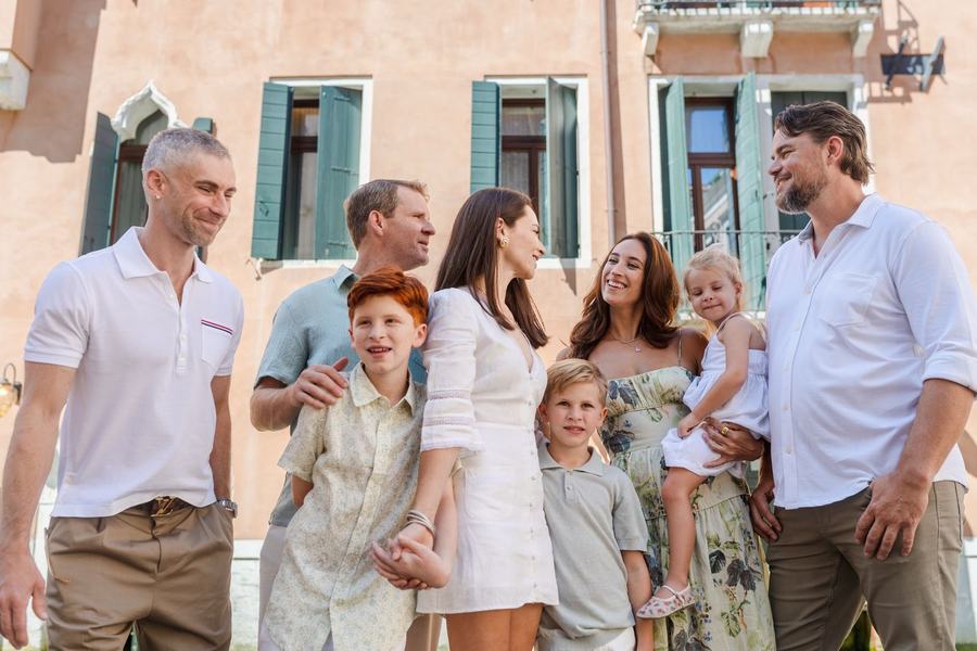 A large family laughing together in front of a peach-coloured Venetian house with green shutters