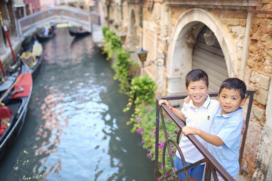 Two brothers leaning on a railing above a canal in Venice