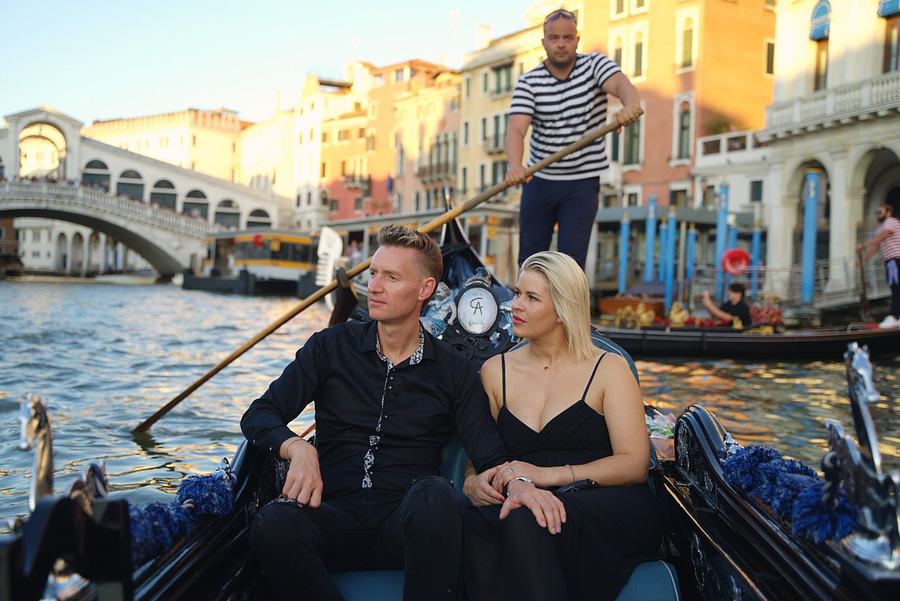 A couple on a gondola at dusk on the Grand Canal, the Rialto Bridge behind them