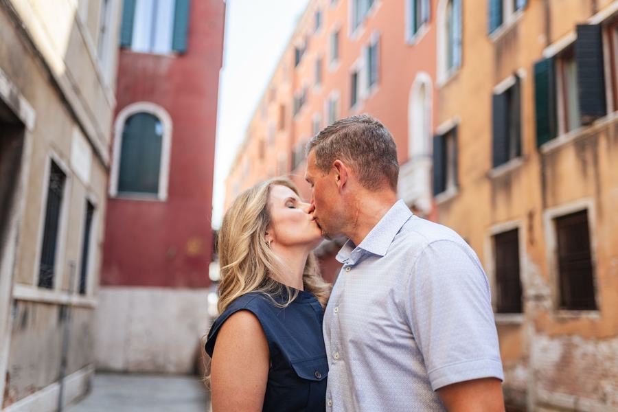 A couple kissing in a quiet Venetian street, a red house behind them