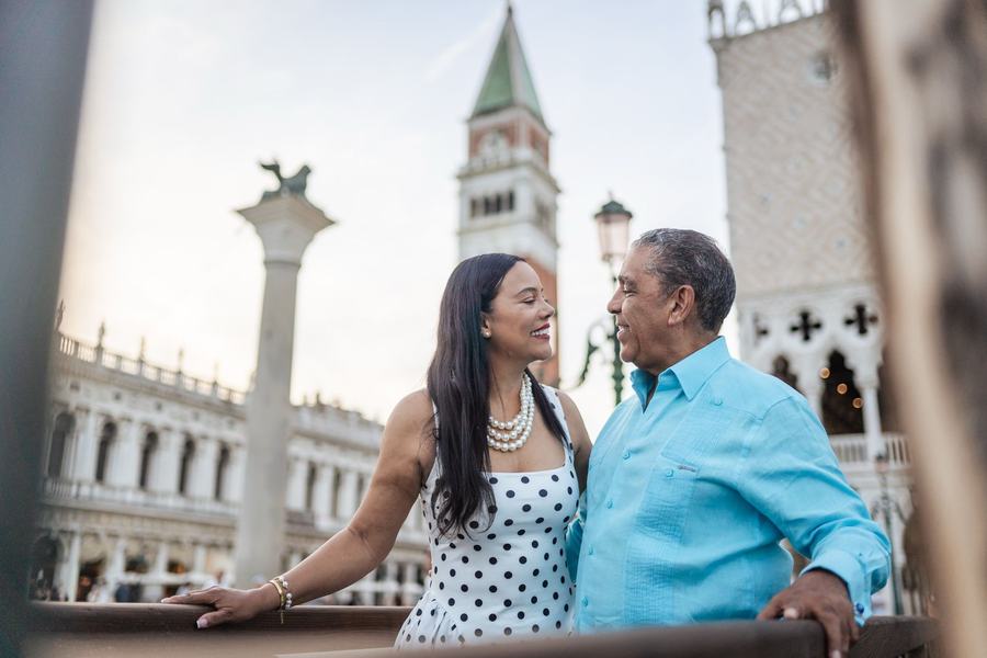 A couple smiling at each other by the column of St Mark's lion, the bell tower behind them