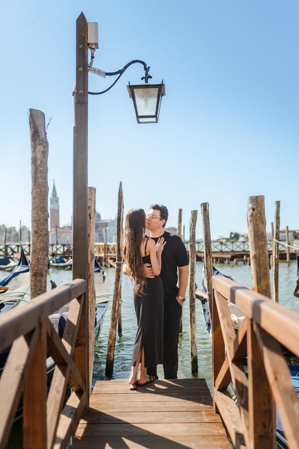 A couple kissing on a wooden pier below a lantern