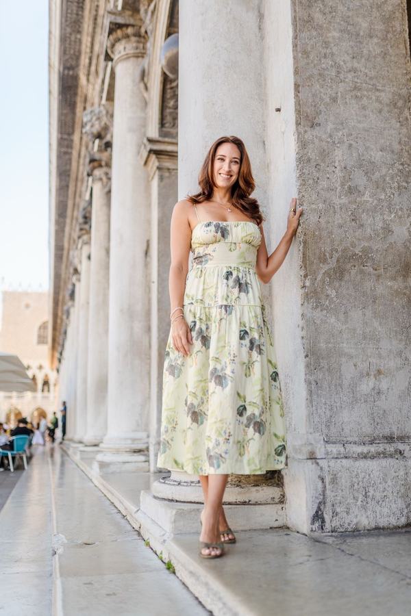 A woman in a floral summer dress leaning against a stone column in St Mark's Square