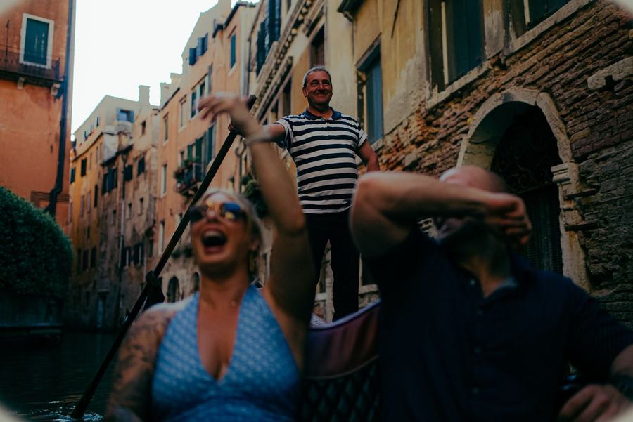 A couple laughing on a gondola ride while the gondolier smiles behind them