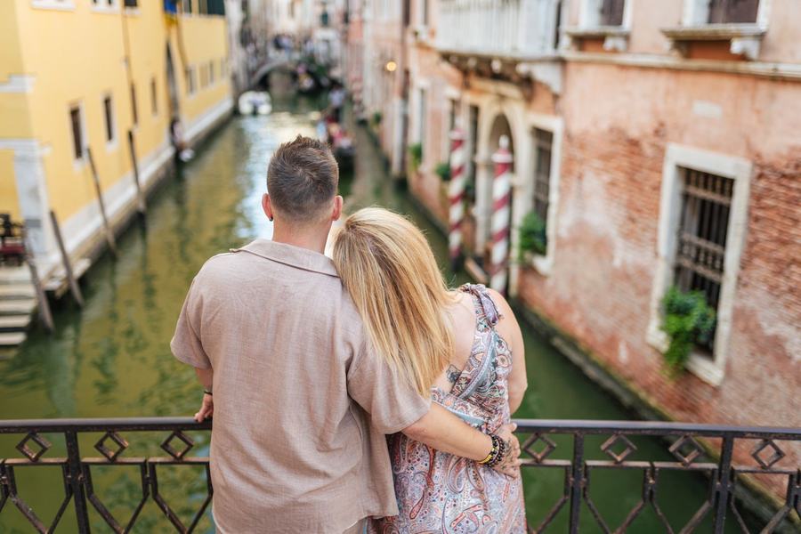 A couple seen from behind, leaning on a bridge railing and looking down a canal