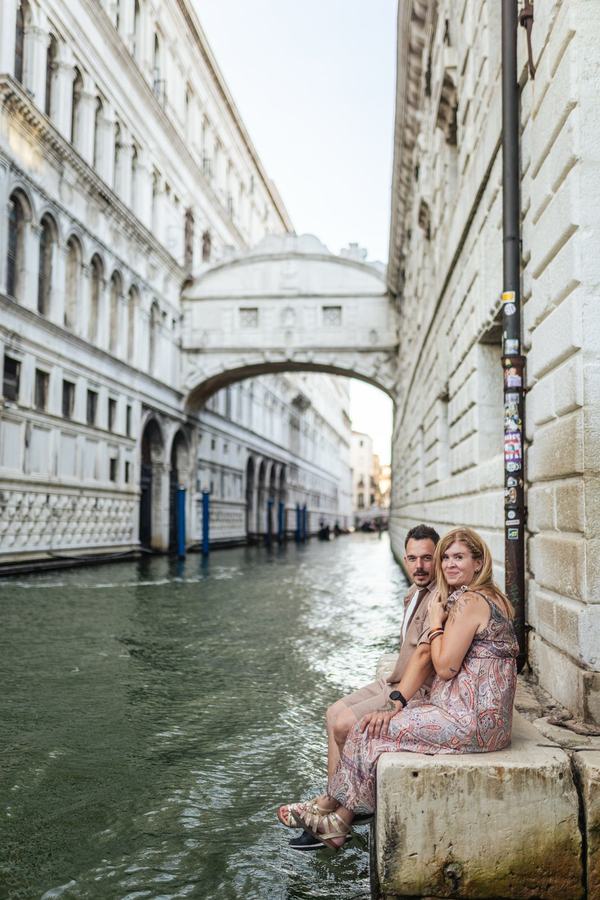 A couple sitting on the canal edge below the Bridge of Sighs