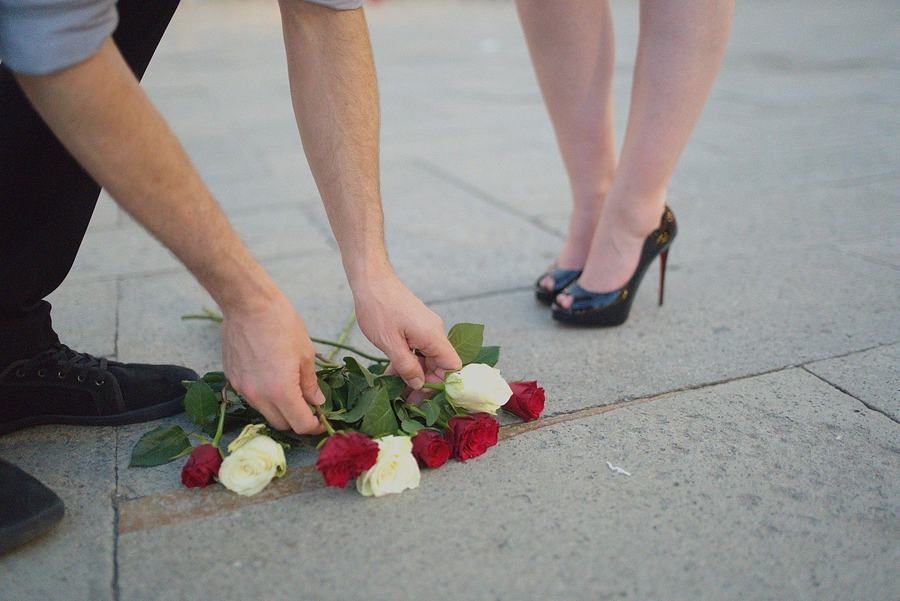 A man laying red and white roses on the stones at a woman's feet