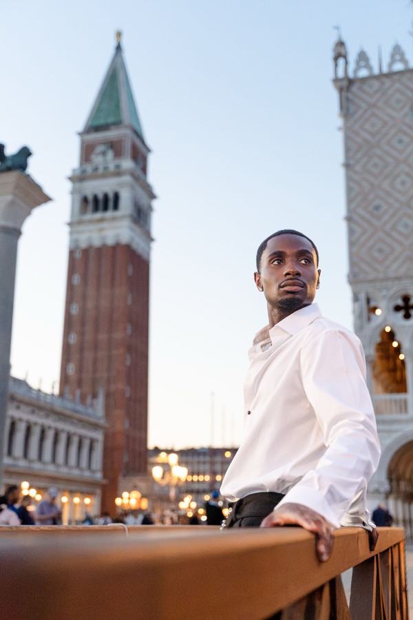 A man in a white shirt at dusk below the bell tower of St Mark's