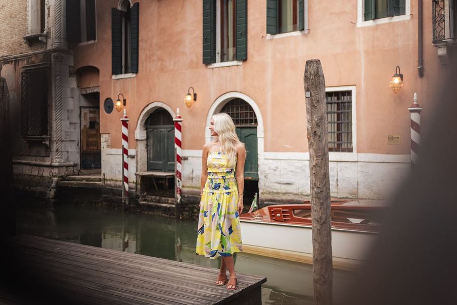 A woman in a yellow dress on a wooden pier by a canal with striped mooring poles